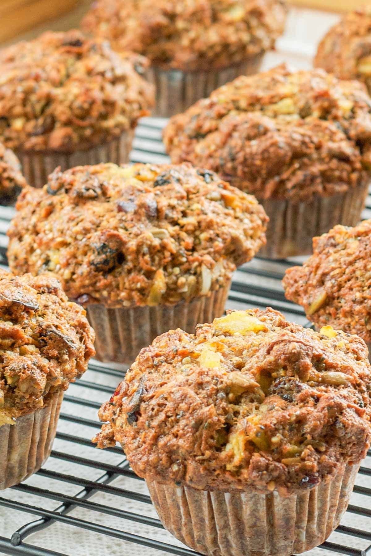 Freshly baked bran muffins cooling on a wire rack. The muffins are golden brown, textured, and packed with visible chunks of fruits and nuts.