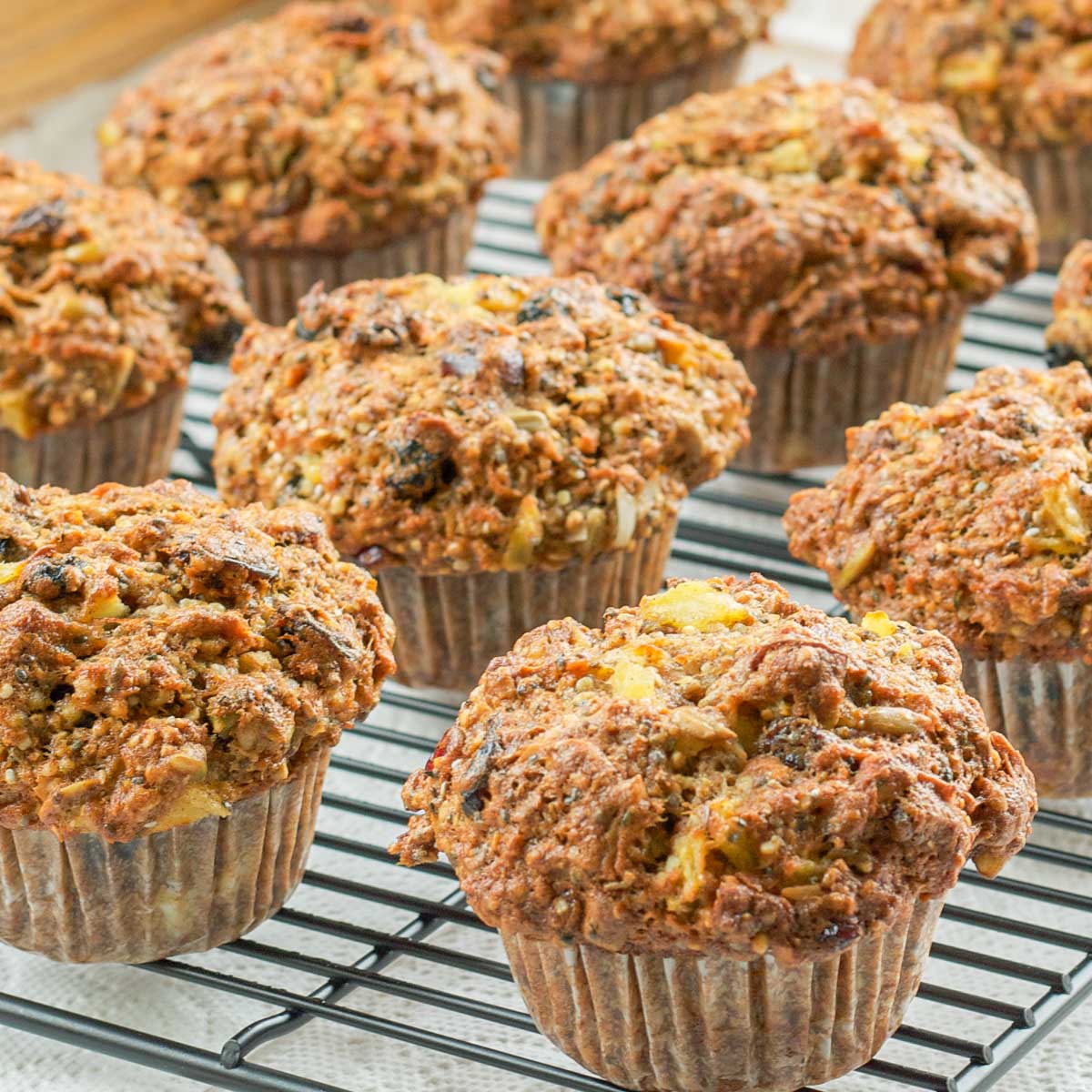 Freshly baked bran muffins cooling on a wire rack. The muffins are golden brown, textured, and packed with visible chunks of fruits and nuts.