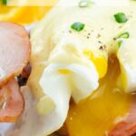 Eggs Benedict with Canadian bacon on toasted muffins, topped with Hollandaise sauce, garnished with chopped chives. Orange slices and parsley on the side. Text reads "Easy Eggs Benedict with blender hollandaise."
