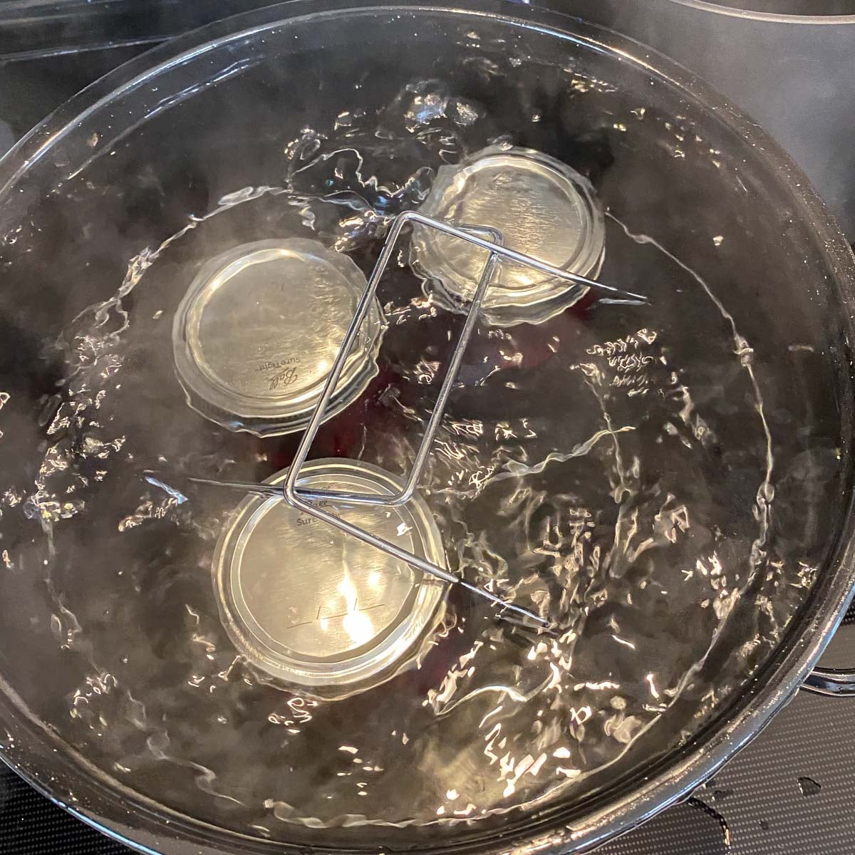 Three jars immersed in a canner of boiling water.