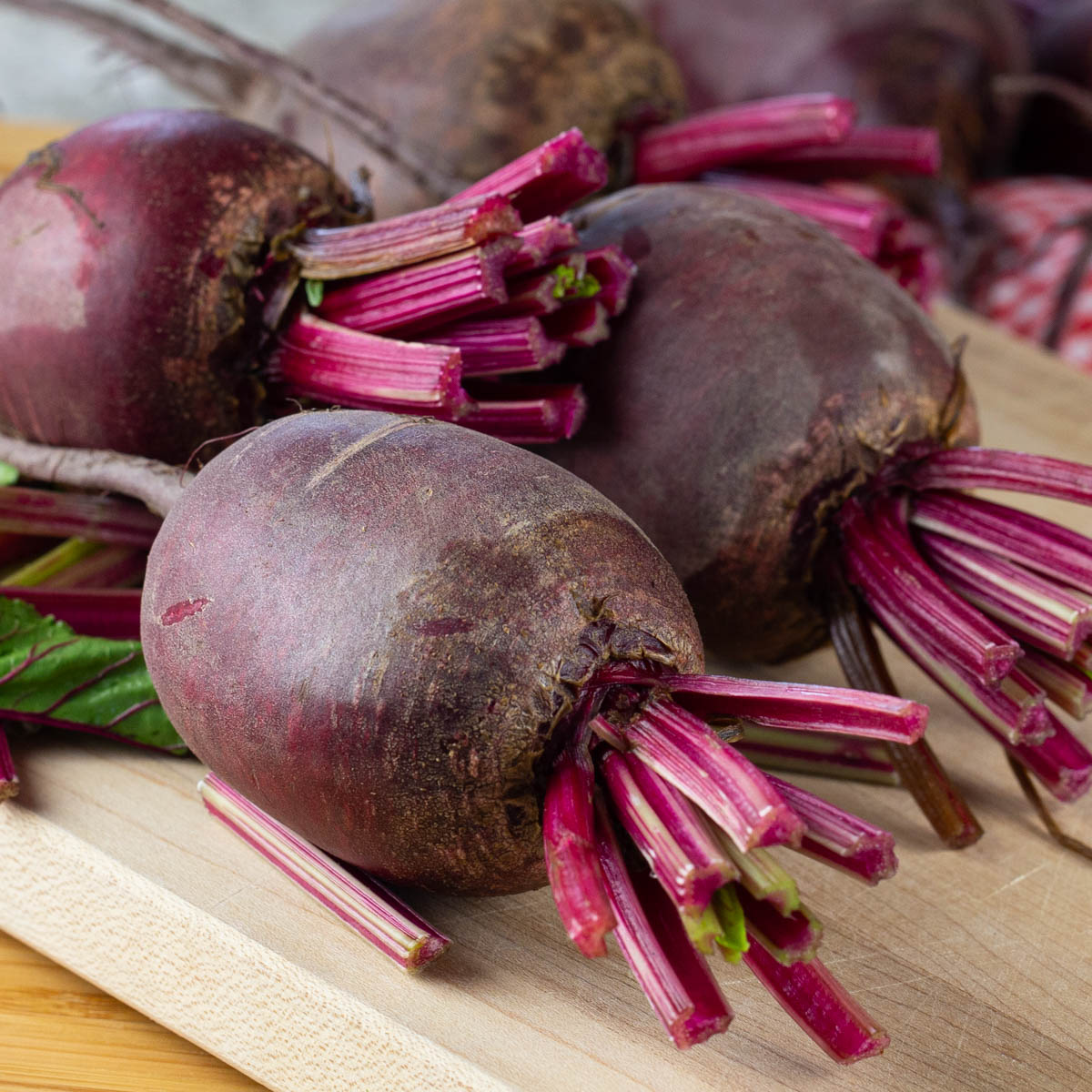 Three fresh beets with green cut off on a wood board.