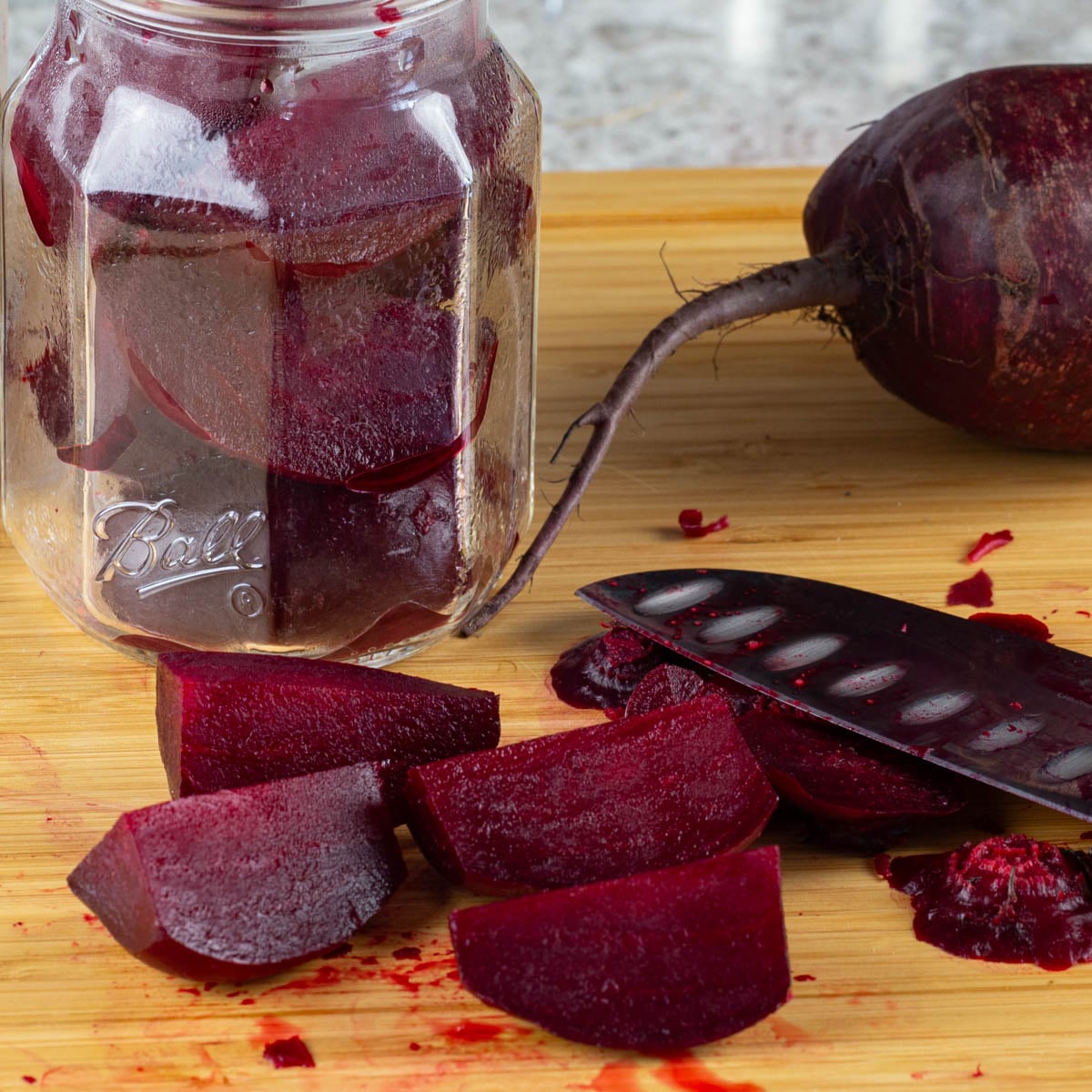 Cubed beets along side of a knife with jar filled with beets and whole beet in the background.