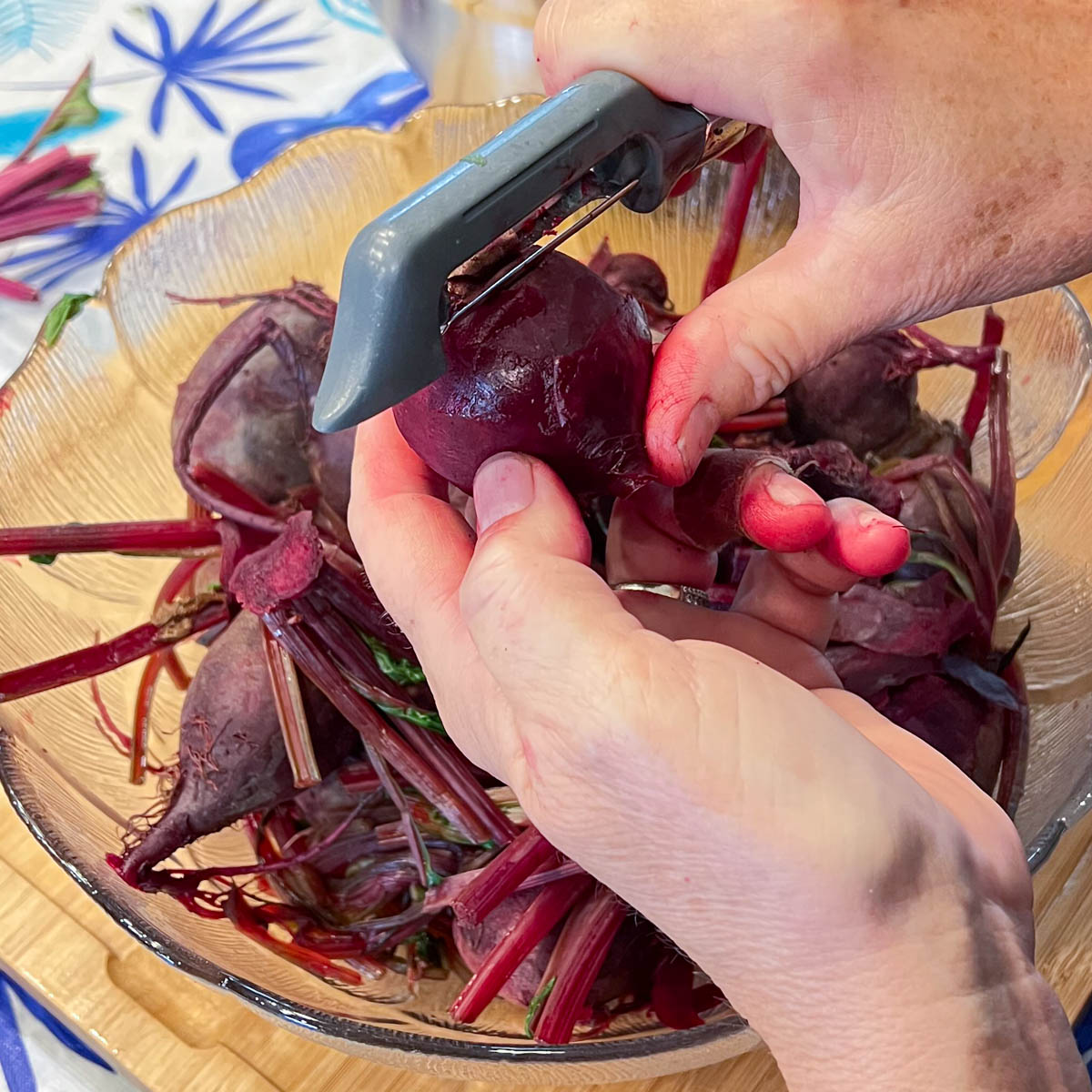 Closeup showing hand peeling beets with vegetable peeler.