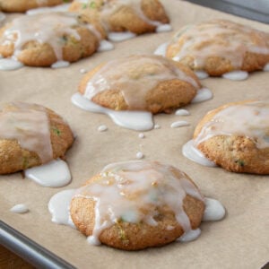Golden zucchini cookies topped with white glaze dripping over the edges, on a parchment-lined baking sheet.