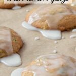 Golden zucchini cookies topped with white glaze dripping over the edges, on a parchment-lined baking sheet.